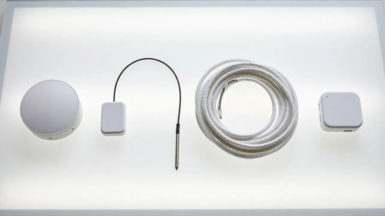 Flat-lay of flood sensor types: spot puck, probe-cable sensor, coiled leak rope and a small hub